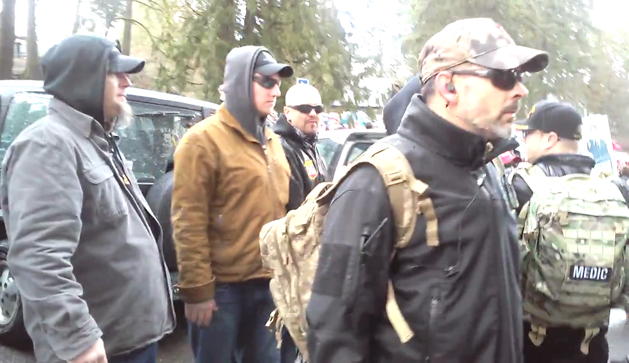 III% Militia members are seen protecting KKK Imperial Wizard and National Socialist Movement member Steven Shane Howard at a far right Trump Rally on 3/4/2017