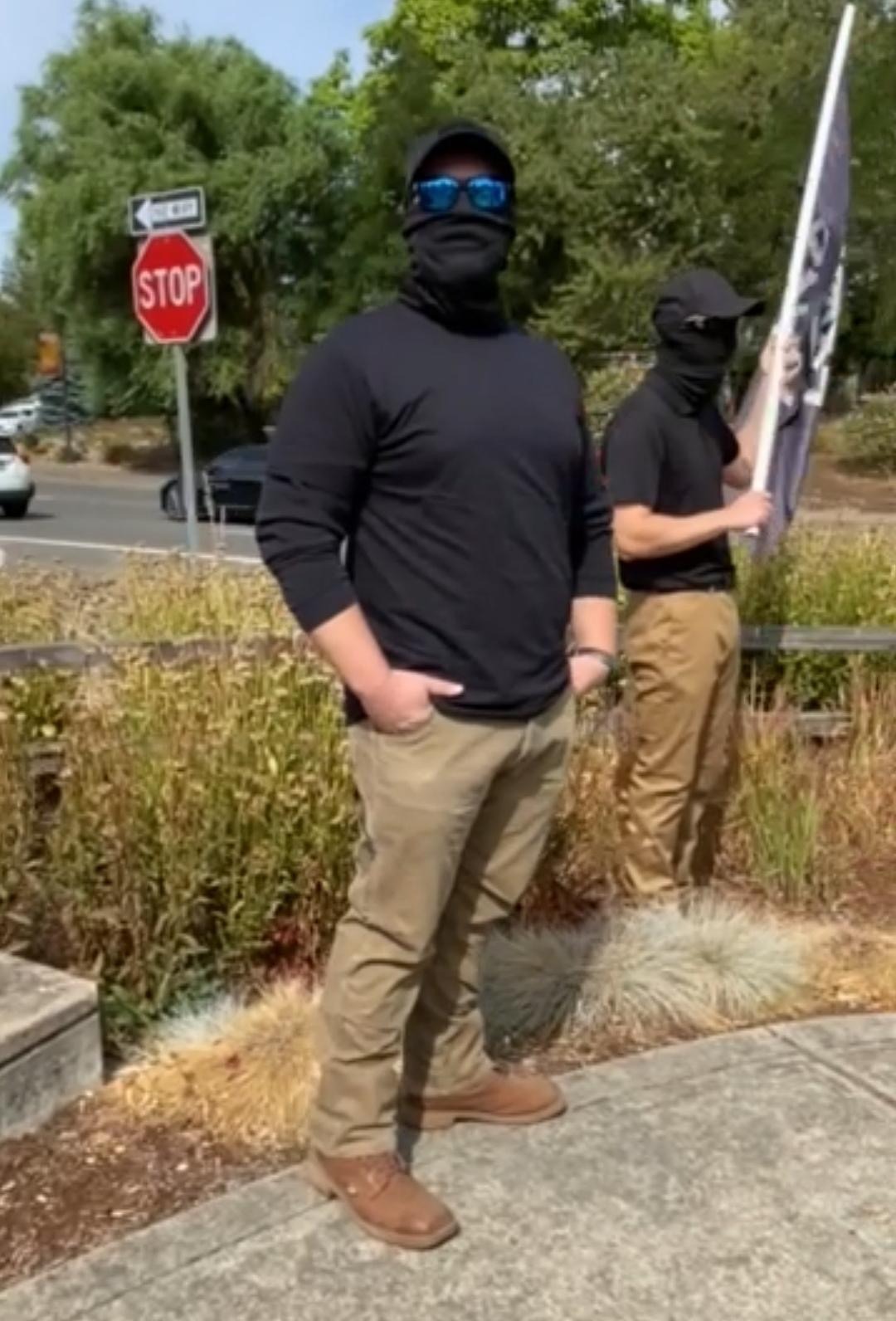 Erick with blue sunglasses and a covered face, standing next to another RCN member holding a sonnenrad flag