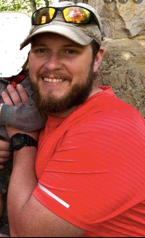 picture of Erick standing in front of a rock wall while holding a child with face blanked out